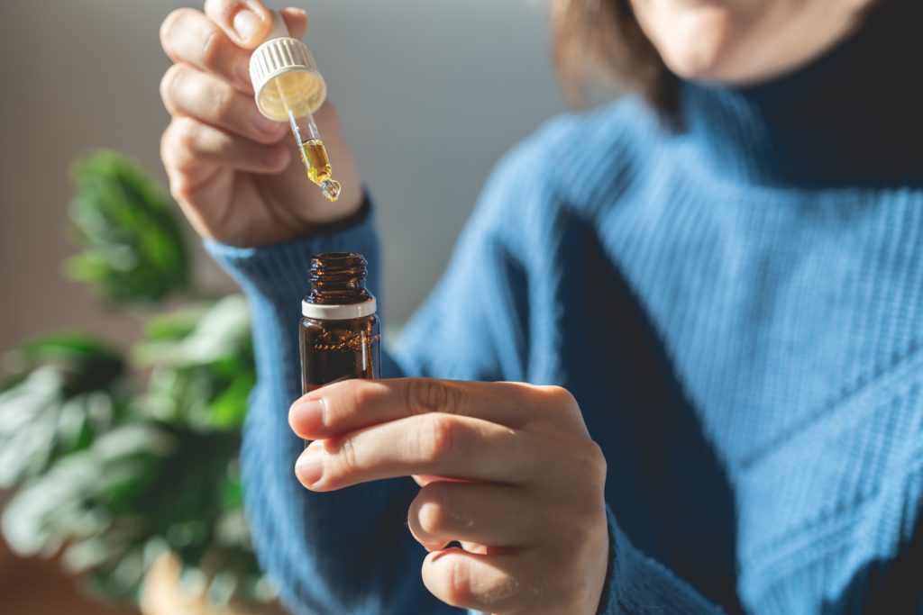 A closeup of a woman from the neck down wearing a blue sweater squeezing tincture into a small brown bottle